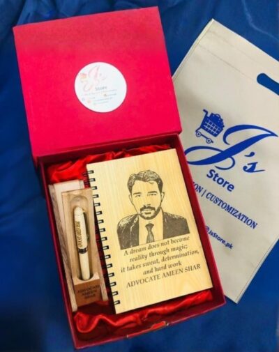 Open red gift box containing a personalized Customized Wooden Notebook Set. The wooden notebook has a laser-engraved portrait and quote, accompanied by a custom wooden pen and stand.