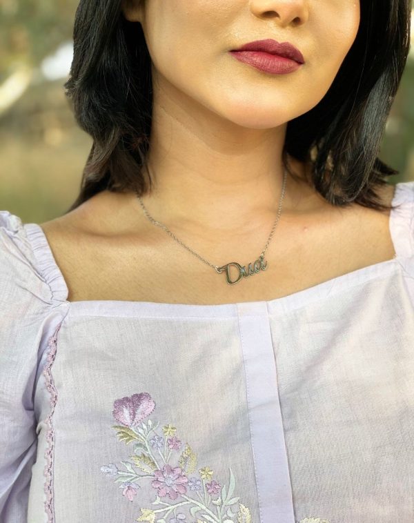 Close-up of Dua's neck, focusing on the Single Name Silver-Plated Necklace, square neck of her dress, and collarbones.