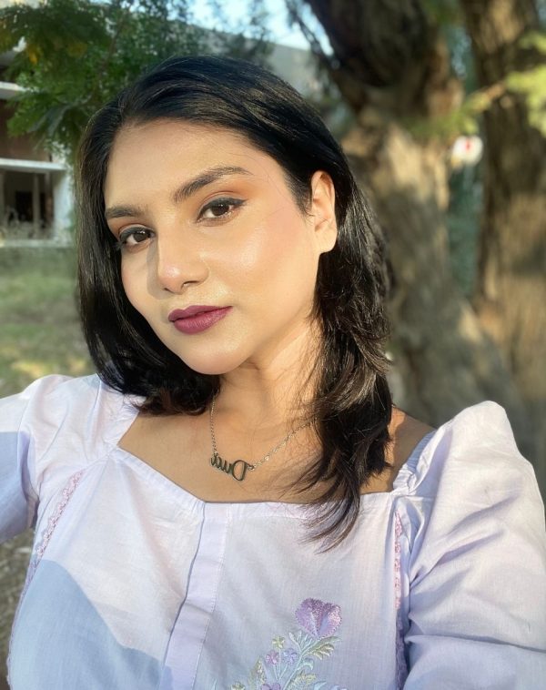 Dua's close-up selfie wearing the Single Name Silver-Plated Necklace, against a backdrop of trees and a distant building, showcasing her stylish outfit and personalized necklace.