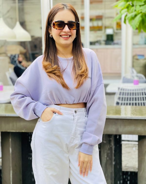 Close-up of Influencer Palvi Ramani wearing Lilac Cropped Drop Shoulder Scannable Sweatshirt, paired with White Jeans. Scannable Spotify code on the sweatshirt. Palvi poses with Cheetah Printed sunglasses in a cafe-like ambiance.