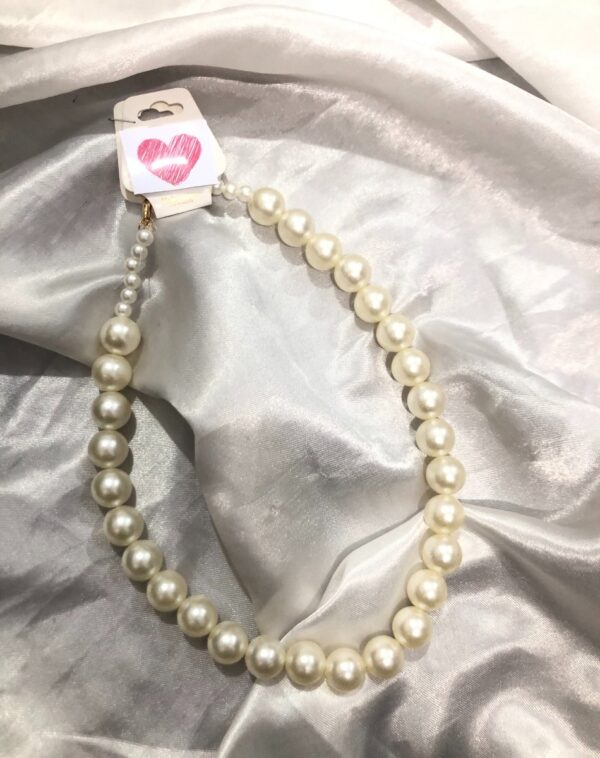 Classic Pearl Necklace: A string of lustrous, cream-colored pearls. The necklace is displayed on a soft, white, satin-like fabric. A small tag with a pink heart is attached near the clasp. This might be a Mikimoto Pearl Necklace.