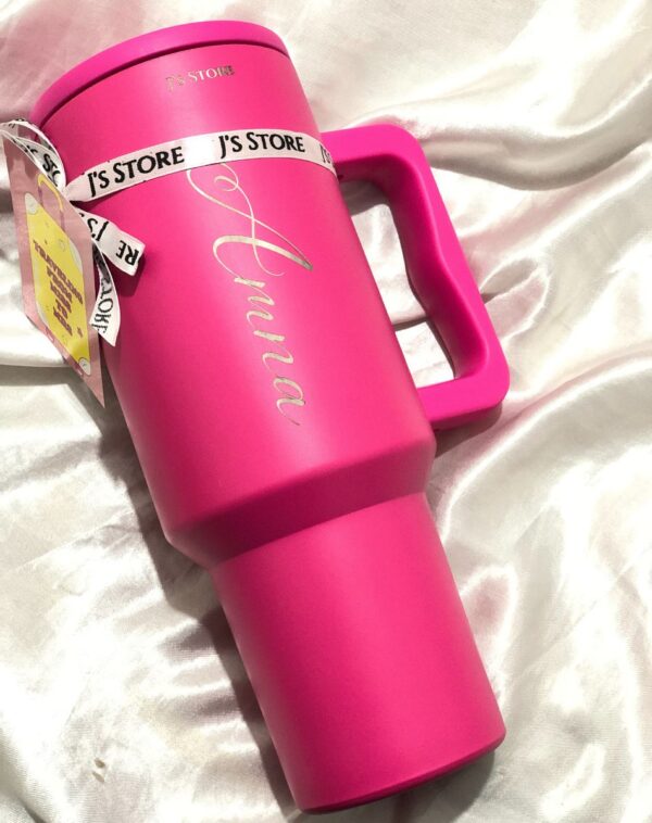 A pink J's Store Quencher Tumbler with the name "Amna" engraved on it