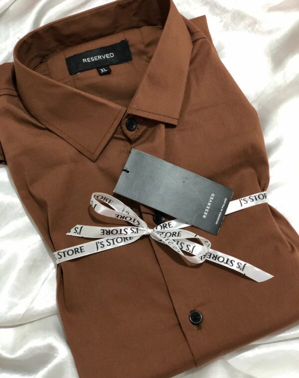 A neatly folded brown plain semi-formal shirt from the brand 'Reserved'. It is tied with a white J's Store ribbon.