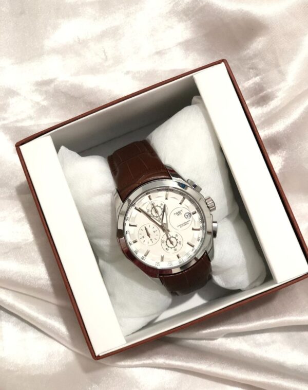 The SuperSport Chrono Watch in a box. The watch has a white face with silver and black dials and a brown leather strap.