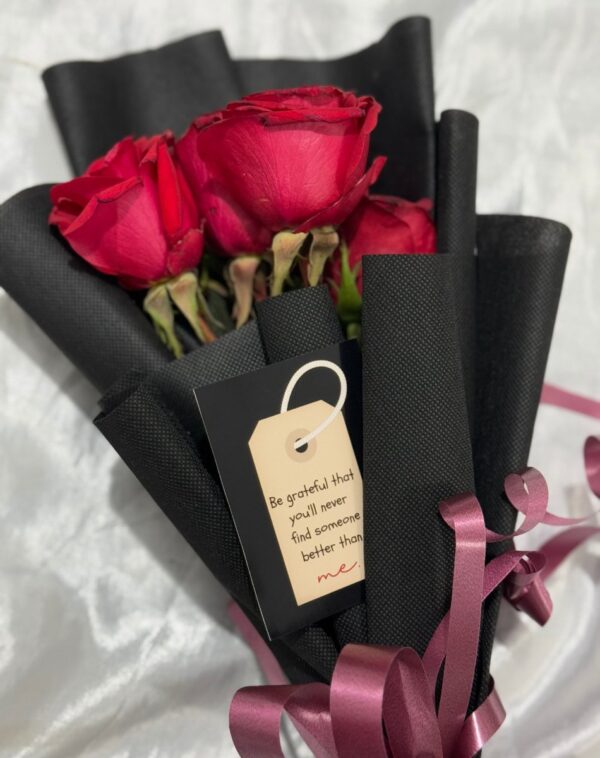A stunning bouquet of deep red roses titled The Eternity Petals by J’s Store, wrapped in elegant black fabric with a witty gift tag.